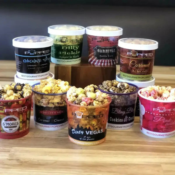 Gourmet popcorn tin collection featuring various flavors and designs, including ’dirty vegas’ and ’cookies & cream.’