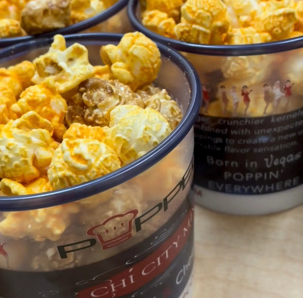 Clear plastic container with navy blue rim and black label featuring a red chef’s hat logo, filled with golden caramel-coated popcorn.