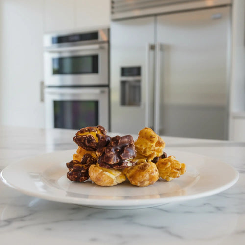 A pile of crunch nato chocolate gourmet popcorn with golden caramel and dark chocolate on a white ceramic plate