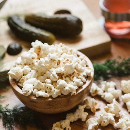 A wooden bowl filled with fluffy white popcorn, some kernels lightly speckled with seasoning.