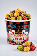 A cup of Popped Dirty Vegas gourmet popcorn filled with multicolored popcorn pieces, with a few pieces scattered in front on a light gray background.