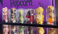 A variety of flavored popcorn and candies in clear cylindrical containers.