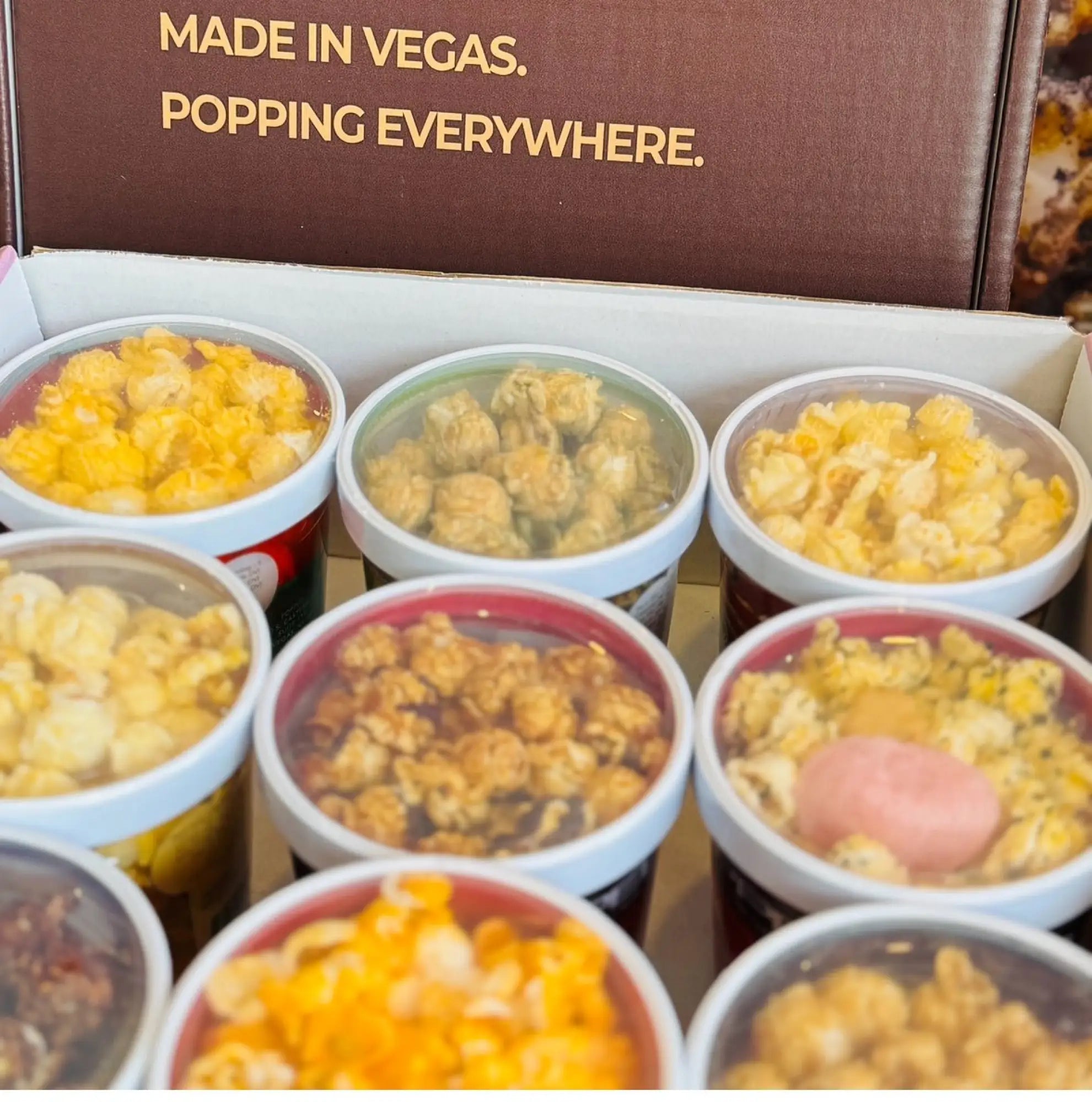 A box of assorted gourmet popcorn in individual clear containers.