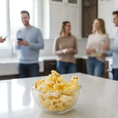 Glass bowl of popcorn on a kitchen counter with people in the background