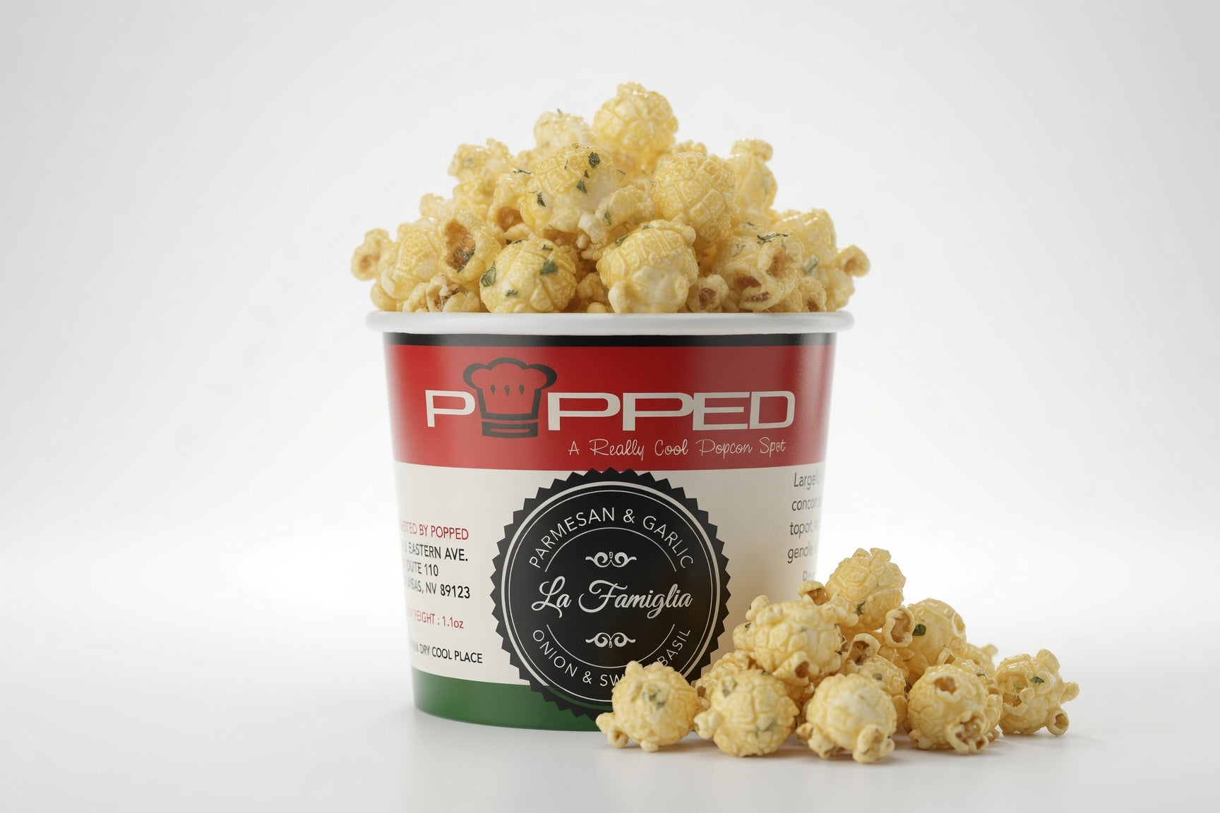 A cup of popcorn with some spilled around the base on a clean white background. The cup has a red, white, and green label with the brand name 'Popped' and a circular badge reading 'Parmesan & Garlic'.