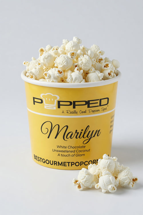 A yellow Popped popcorn bucket filled with white chocolate-flavored popcorn, with a few popcorn kernels placed in front on a light gray background.