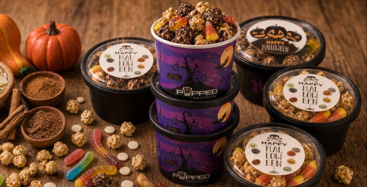 A styled product display of Pippio's 'Happy Fall Popcorn' tubs and bags on a rustic wooden table, surrounded by Halloween-themed ingredients like candy corn, gummy worms, pumpkin seeds, cinnamon, and mini pumpkins.