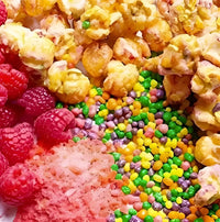 Colorful popcorn with raspberries and rainbow sprinkles on a white plate