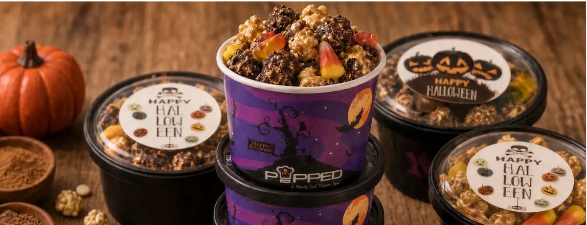 A styled product display of Pippio's 'Happy Fall Popcorn' tubs and bags on a rustic wooden table, surrounded by Halloween-themed ingredients like candy corn, gummy worms, pumpkin seeds, cinnamon, and mini pumpkins.