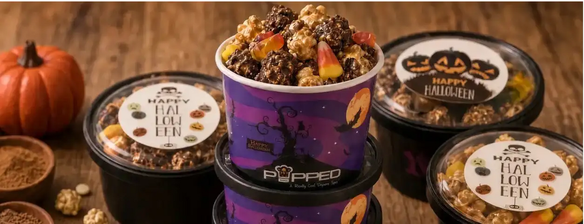 A styled product display of Pippio's 'Happy Fall Popcorn' tubs and bags on a rustic wooden table, surrounded by Halloween-themed ingredients like candy corn, gummy worms, pumpkin seeds, cinnamon, and mini pumpkins.