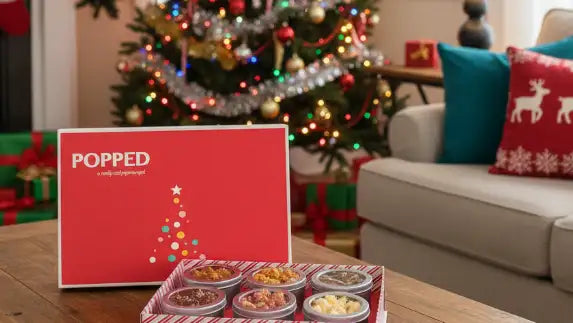 Christmas-themed setting with a 'Popped' product display on a table, decorated tree, and fireplace.