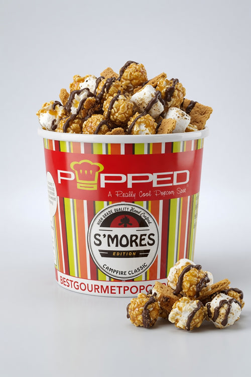 A cup of Popped S'mores gourmet popcorn, filled with caramel popcorn and drizzled with chocolate sauce, with a few pieces resting in front on a light gray background.