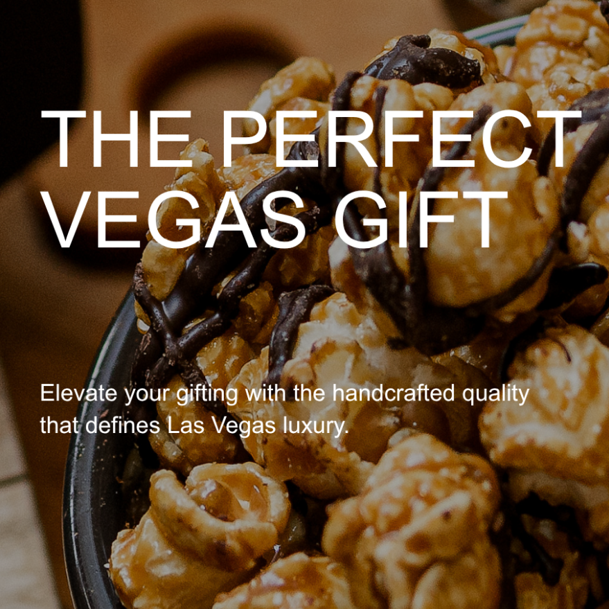 A close-up promotional photo of caramel-coated popcorn with dark chocolate drizzle in a bowl, with overlaid text reading 'THE PERFECT VEGAS GIFT' and smaller copy about handcrafted quality and Las Vegas luxury.