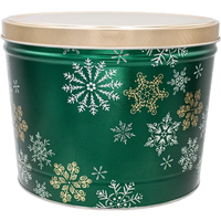 A green cylindrical holiday tin with a gold lid, decorated with white and gold snowflakes.